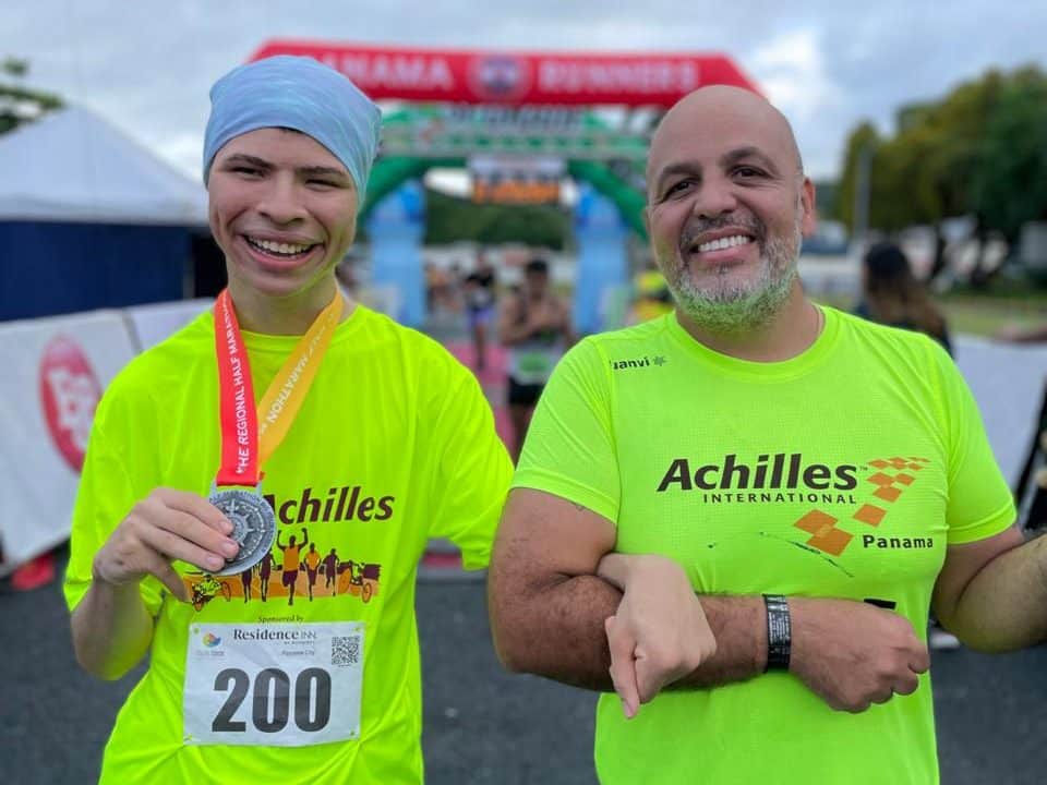 Un atleta con su medalla y su guía bajo el arco de meta